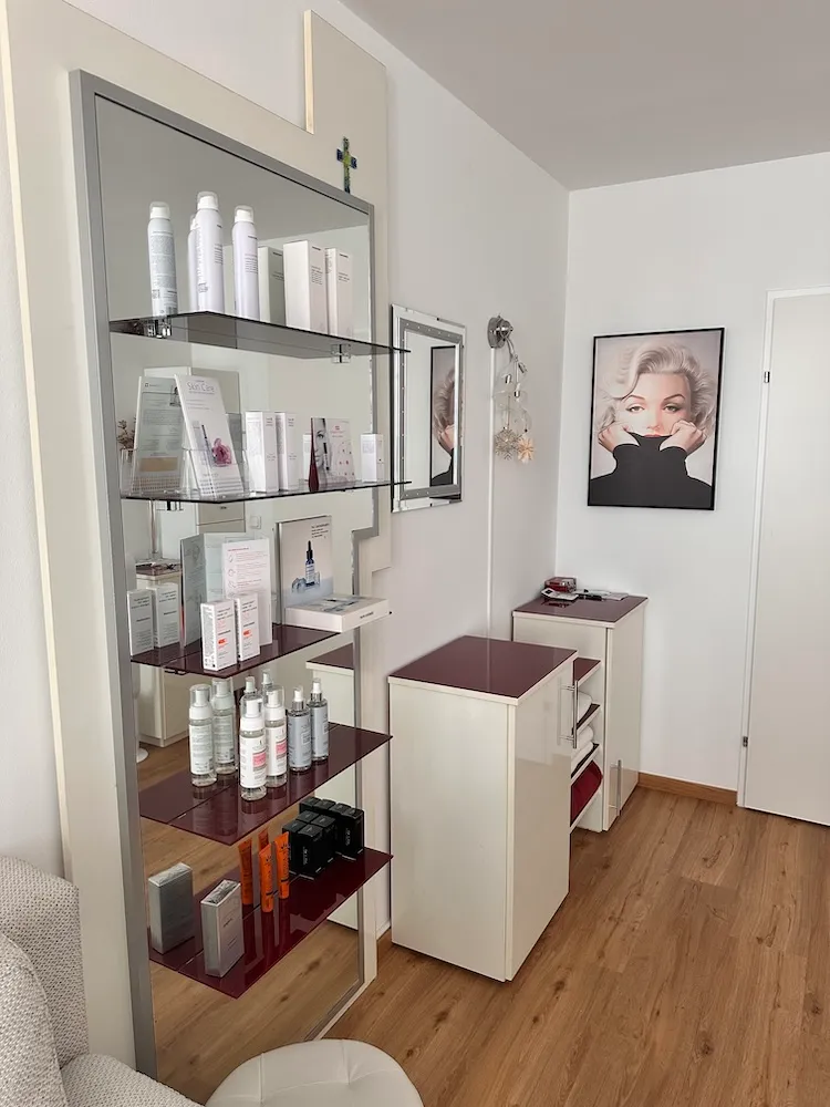Produktregal mit Pflegeserien vor einem Wandspiegel, daneben ein Marilyn-Monroe-Porträt
